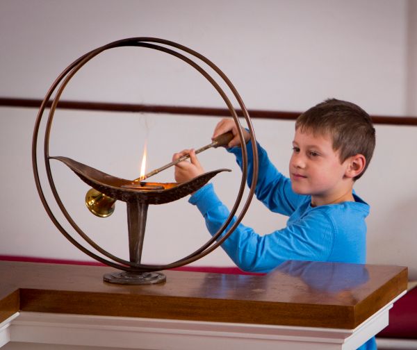 A young boy lighting the flaming chalice
